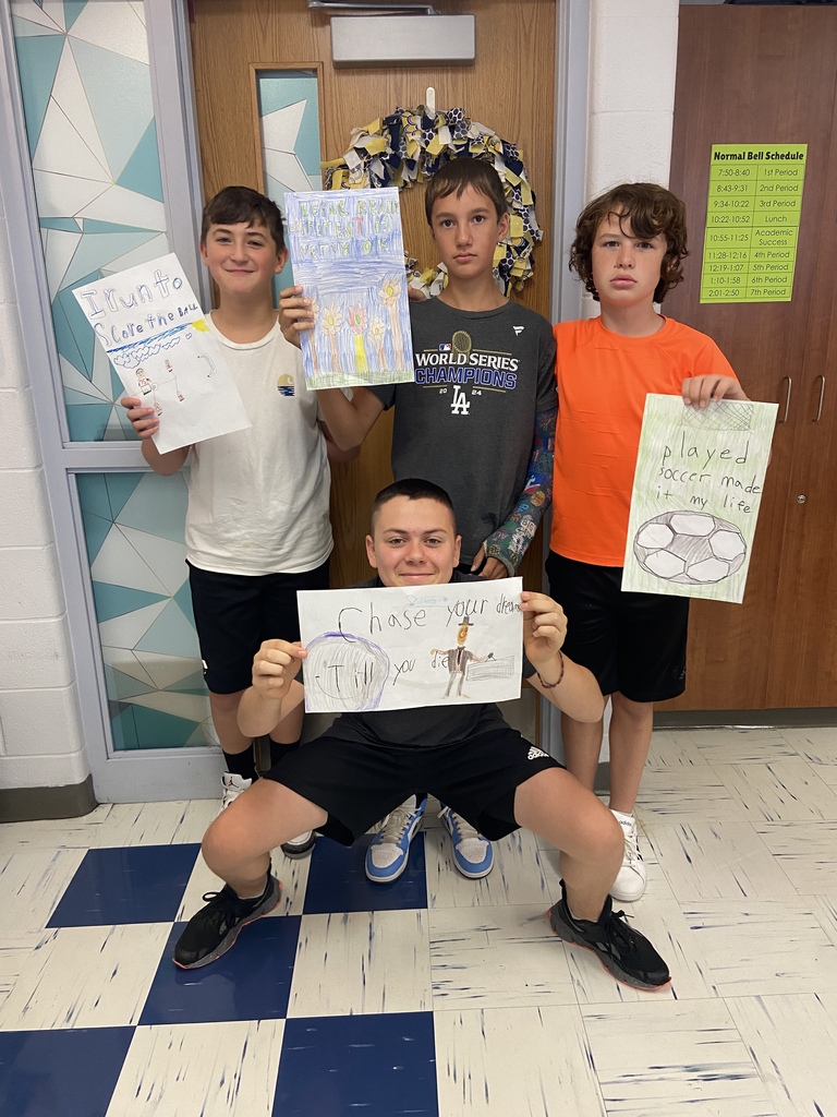 7th grade students hold their posters with their 6 word memoir illustrations in the classroom.