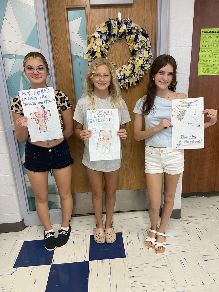 7th grade students hold their posters with their 6 word memoir illustrations in the classroom.