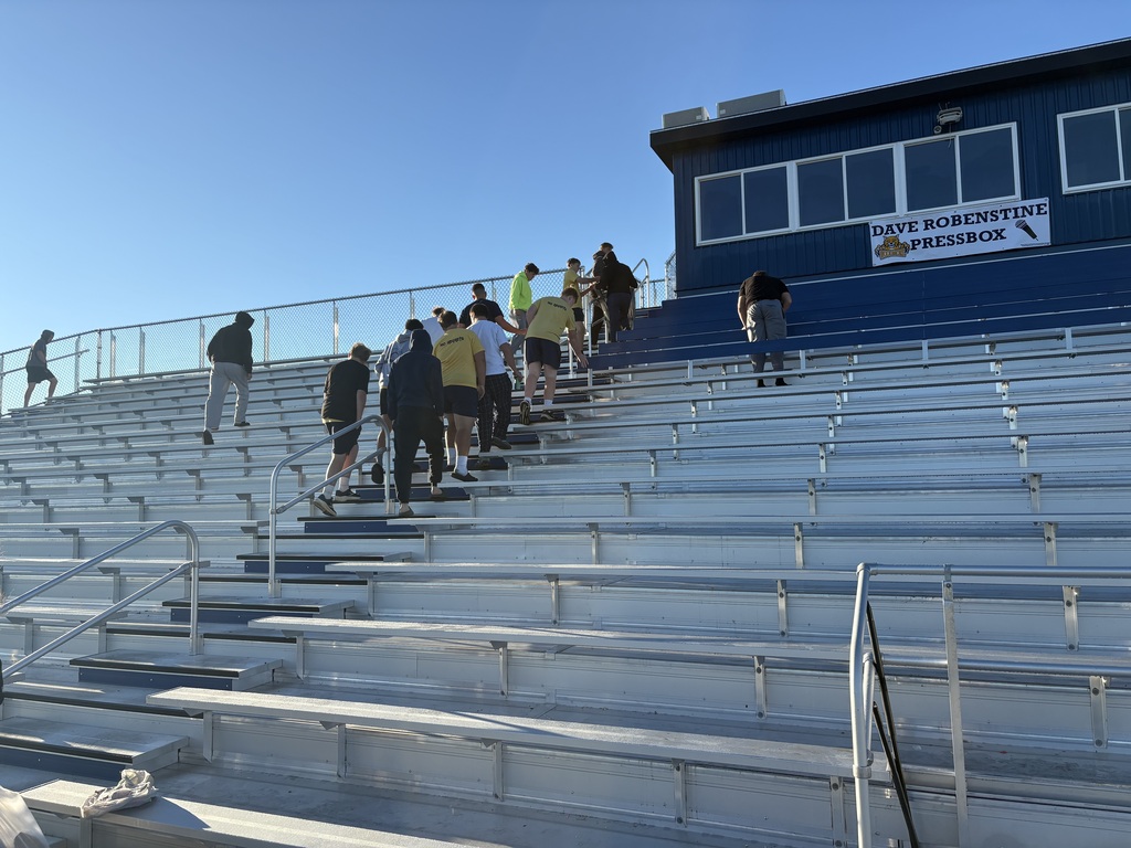 Football players in the stands cleaning up the trash. You can see the new press box in the background.