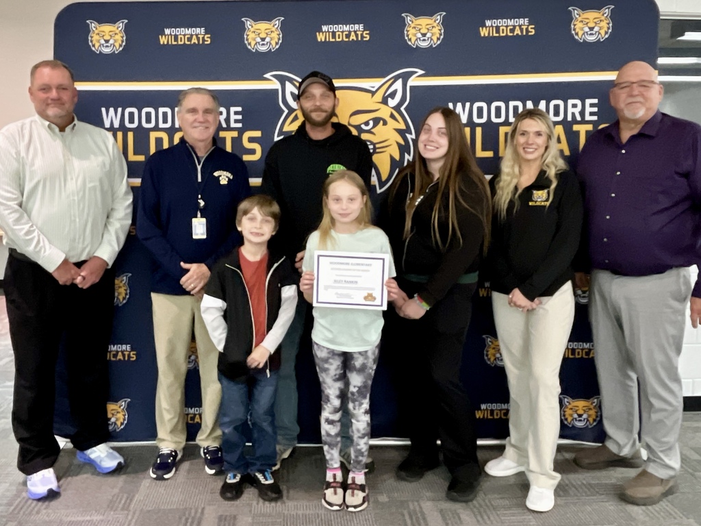 PK-8 Student of the Month pictured with family and district representatives in front of the Woodmore backdrop.