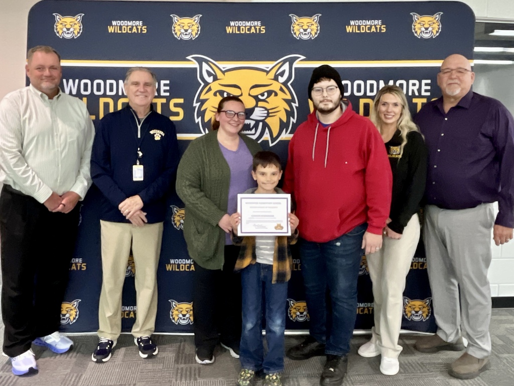 PK-8 Student of the Month pictured with family and district representatives in front of the Woodmore backdrop.