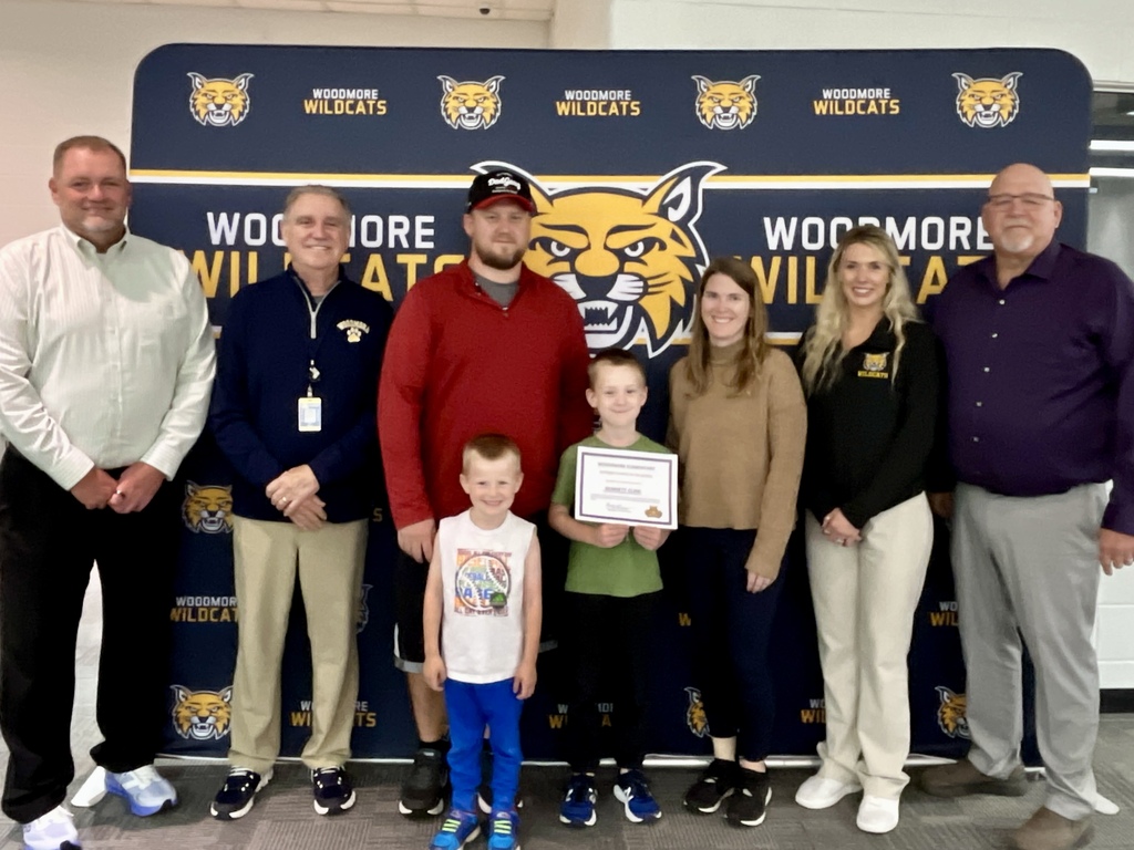 PK-8 Student of the Month pictured with family and district representatives in front of the Woodmore backdrop.