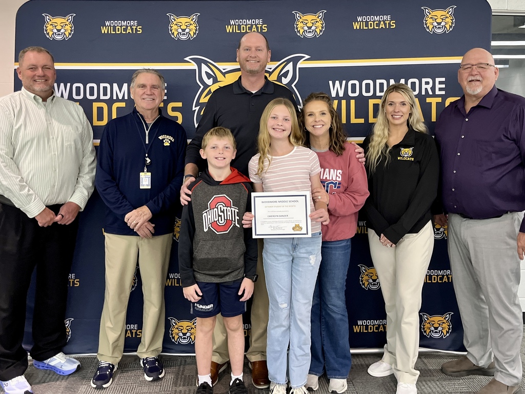 October PK-8 Student of the Month, Emersyn Sander, pictured with family and district representatives in front of the Woodmore backdrop.