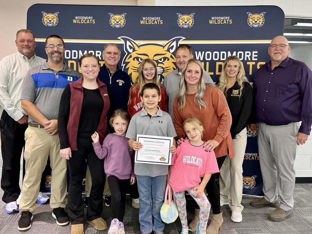 PK-8 student of the month pictured with family and district representatives in front of the Woodmore backdrop.