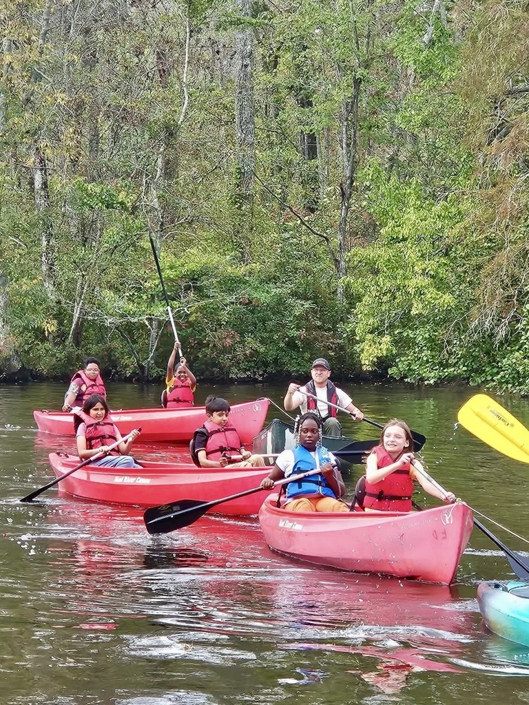 A group of students paddle red canoes together.