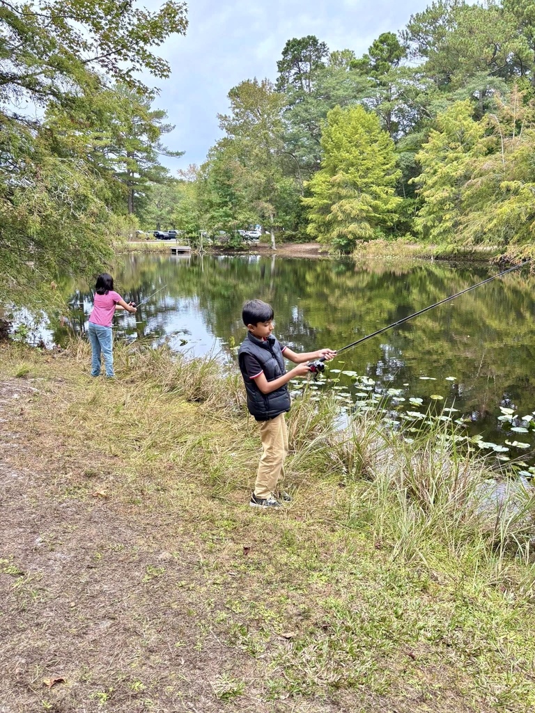 Two students fish along the grassy bank of a pond.