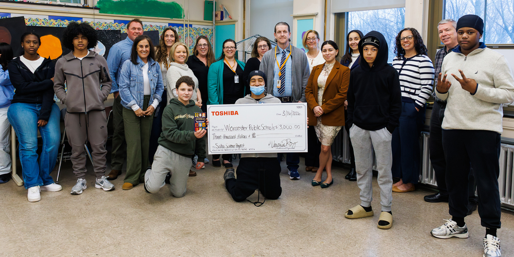 A group of students and adults pose for a photo, holding a large check for $3,000 to Challenge and Reach.