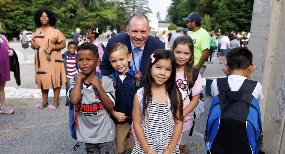 Brian Allen standing with young students in a school playground