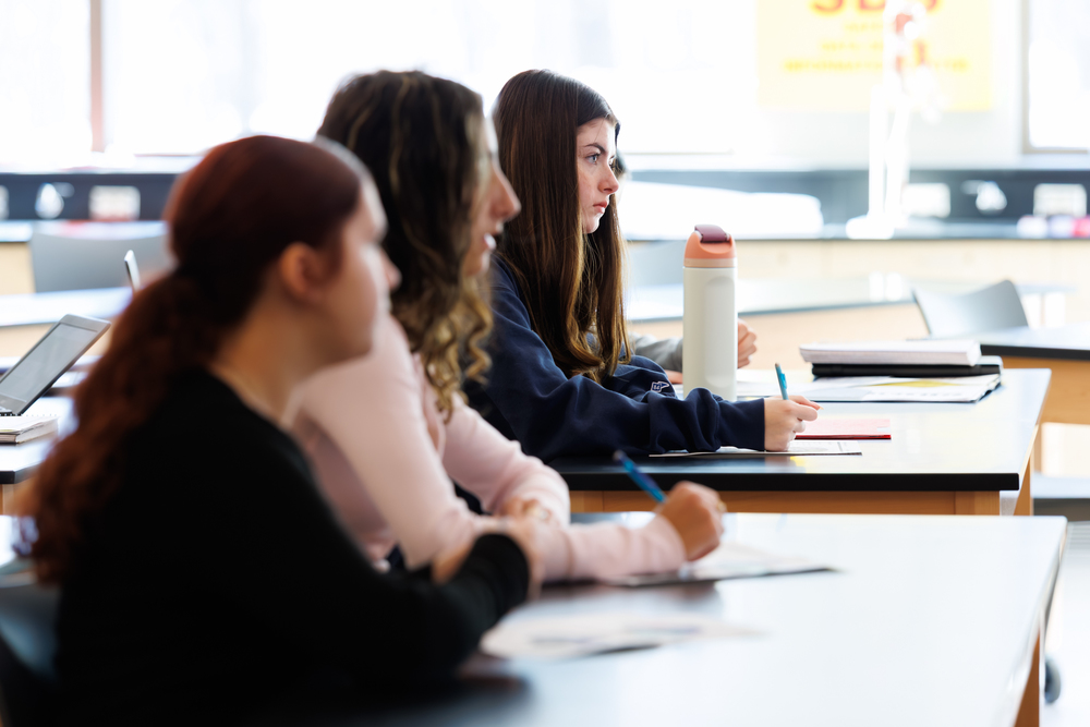 Students attentively listen and take notes in a classroom setting.