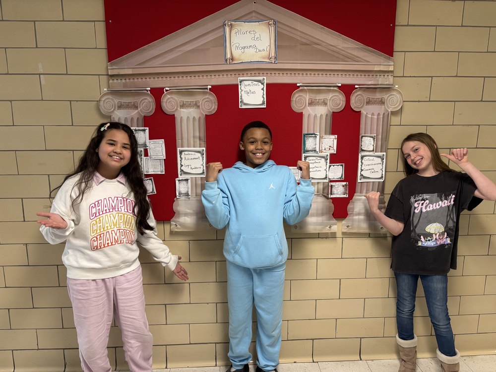 Three students standing in front of a poster outlining the pillars of dual language