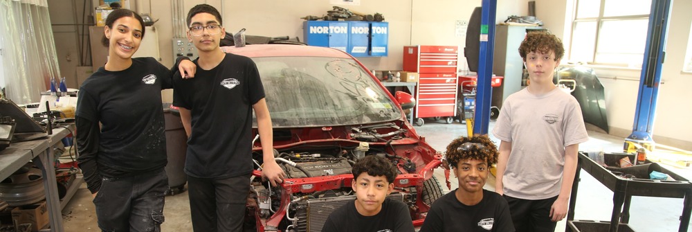 Five students standing in front of a car in a garage