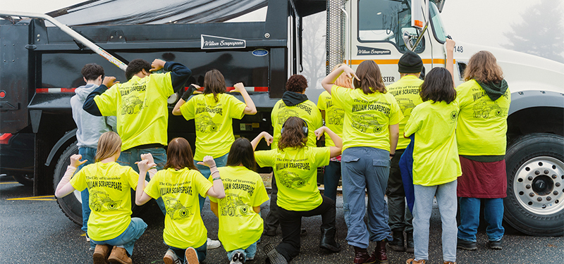 Students wearing t-shirts that say William Scrapespear in front of a snowplow