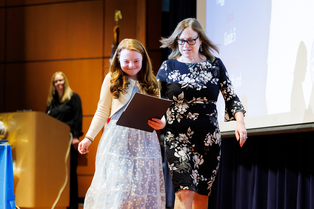 A student walks across the stage during the Celebration of Success alongside an adult.