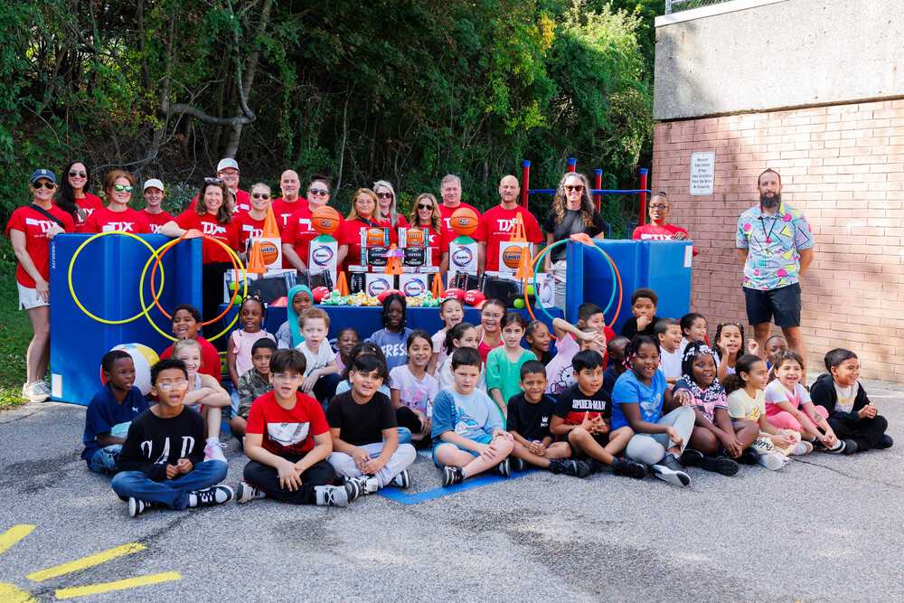 Students and volunteers from TJX stand in front of donated sports equipment.