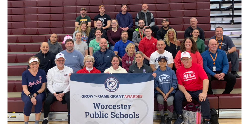 A group of staff members pose for a photo in a gymnasium, proudly holding a banner that reads 'GROW the GAME GRANT AWARDEE Worcester Public Schools.