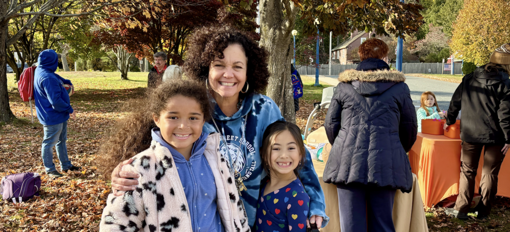 A woman smiling with two girls in a school yard