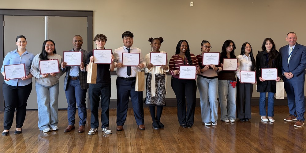A diverse group of young people and an adult man stand in a line, each holding a certificate.