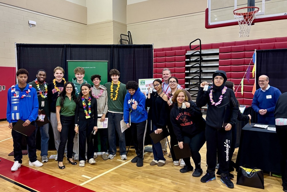 A group of students and adults pose together, some holding certificates, in a gymnasium.