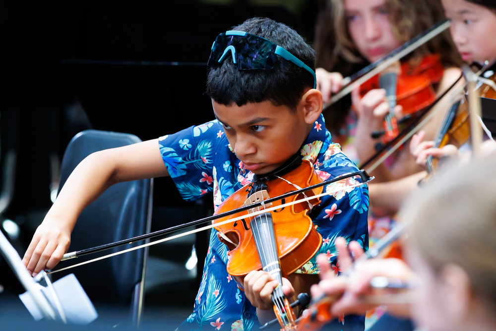 A student wearing a floral shirt focuses while playing the violin.