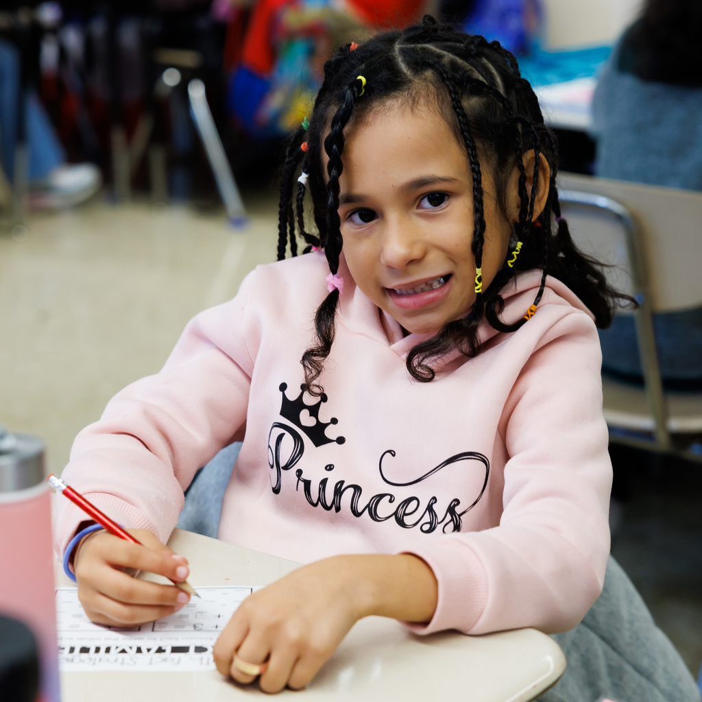 A student smiles at the camera while doing school work.