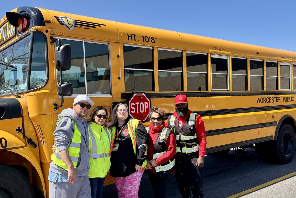 Four people stand in front of a yellow school bus, with the words 'Worcester Public Schools' on the side.