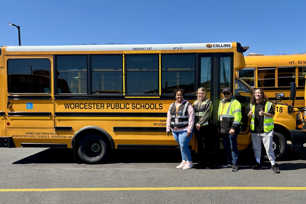 Four people stand in front of a yellow school bus, smiling and looking at the camera. The bus is labeled 'Worcester Public Schools.'