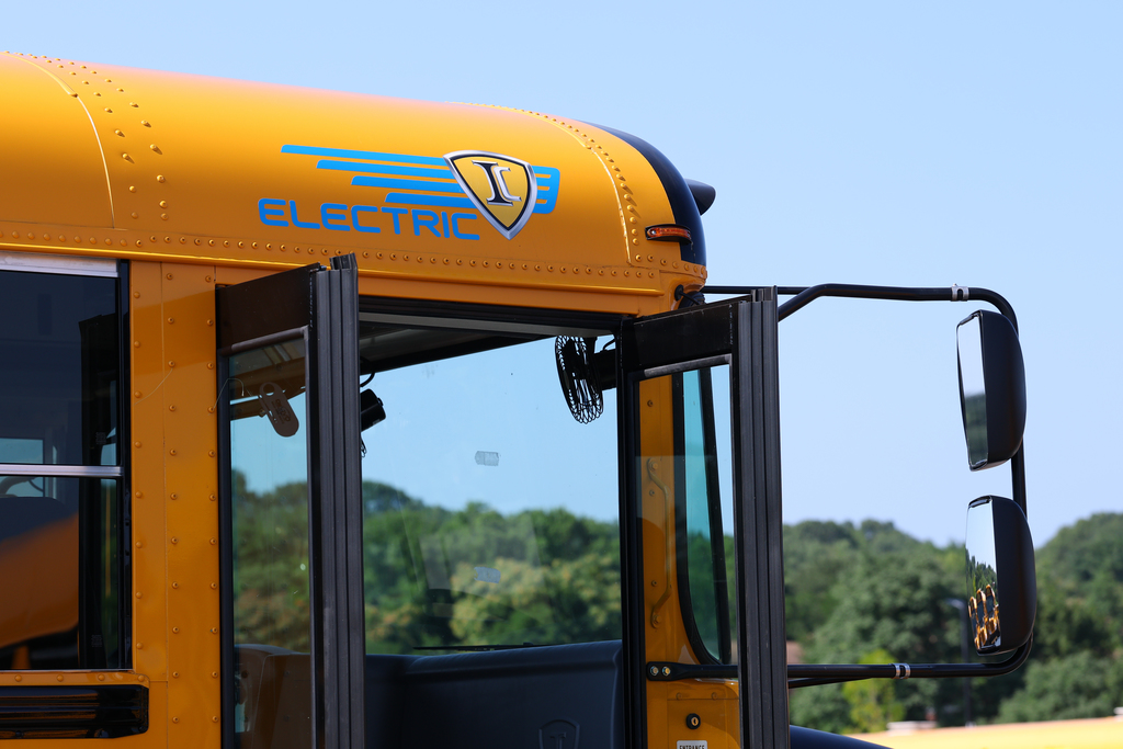 A yellow electric school bus with open doors is parked outdoors.