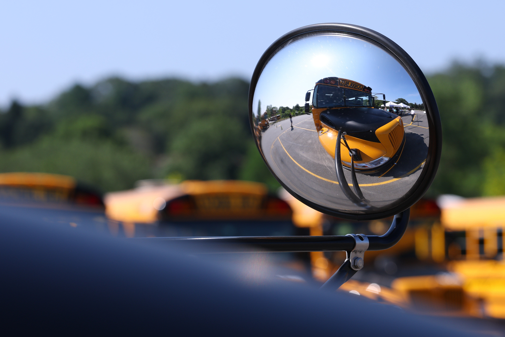 A school bus is reflected in a side mirror, with other buses in the background.