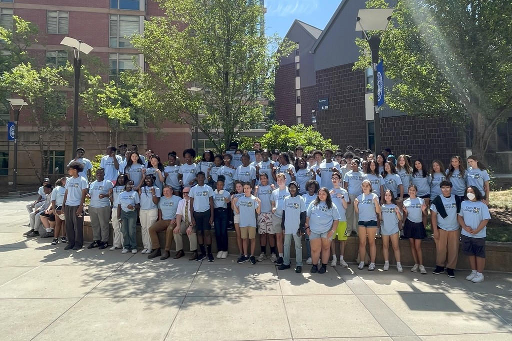A large group of students in light blue t-shirts pose for a photo outdoors.