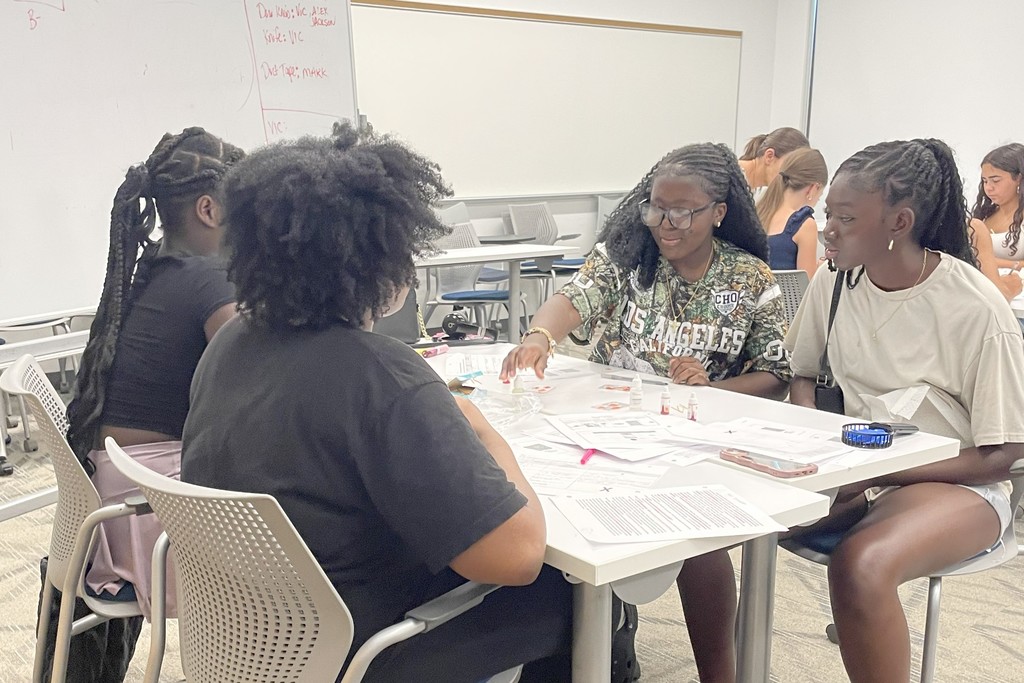 A group of young people collaborate at a table in a classroom setting.