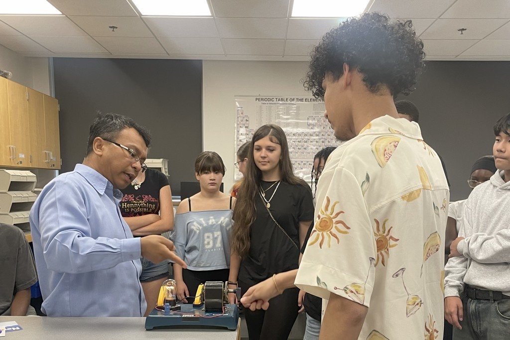 A teacher explains a science experiment to a group of students in a classroom.