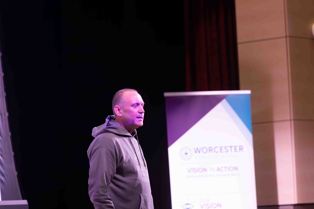 A man in a hoodie stands on a stage, looking to the side.