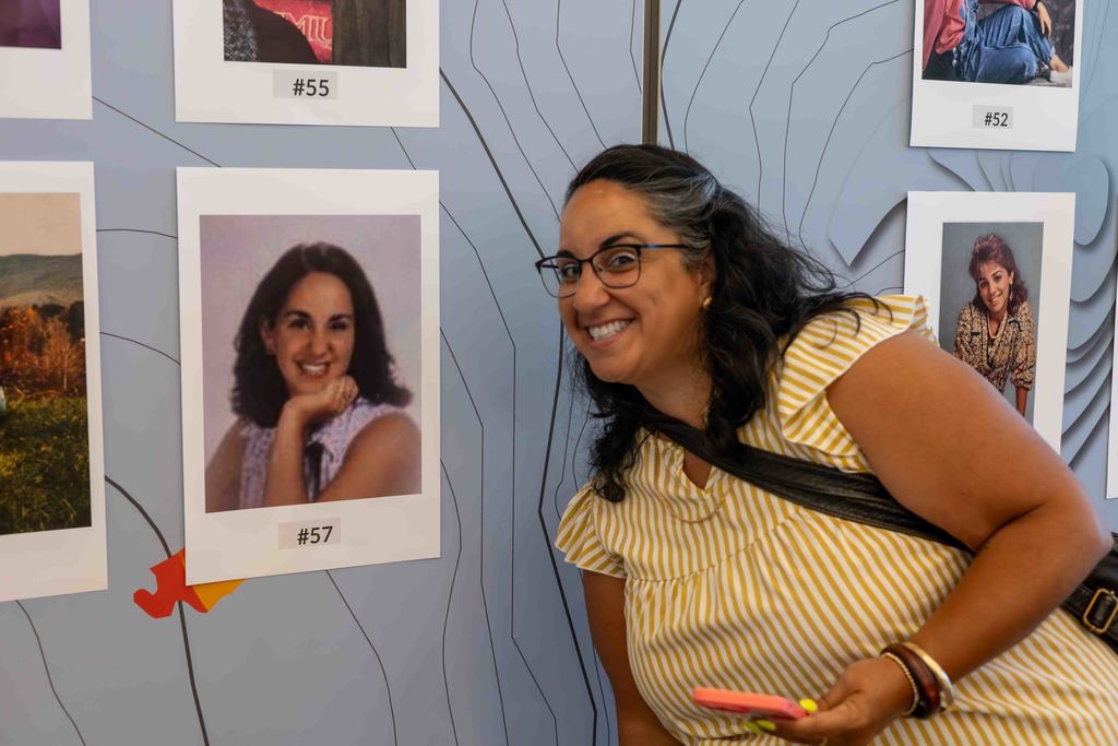 A woman smiles while looking at photos on a wall.