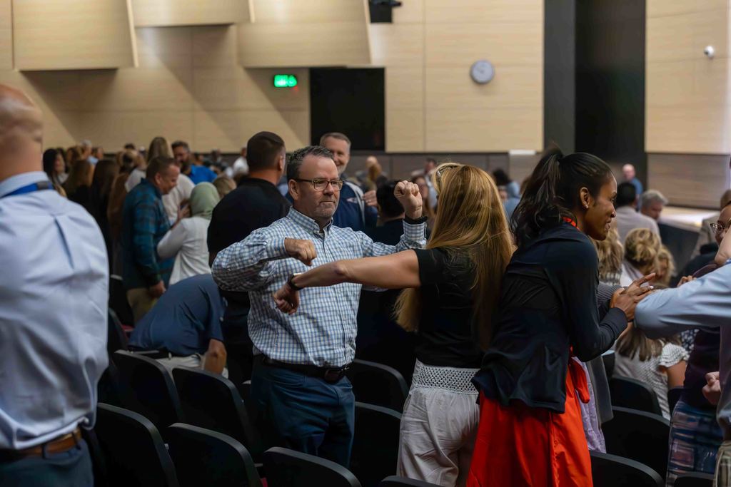 A group of people are in a large room, some are interacting with each other.