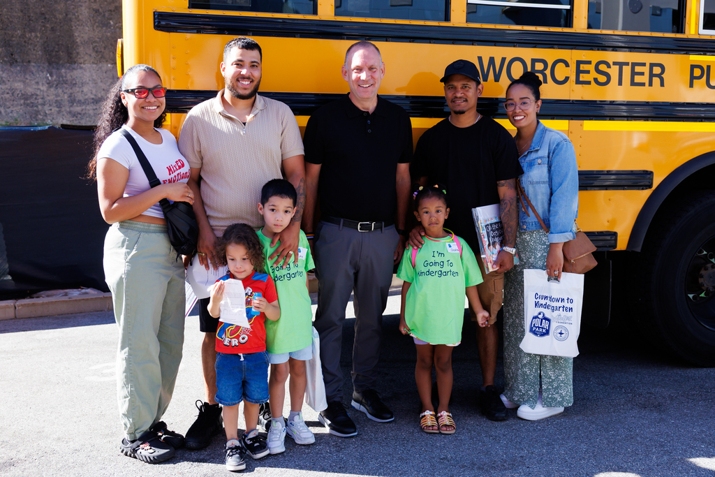 A group of people, including children, pose in front of a yellow school bus.