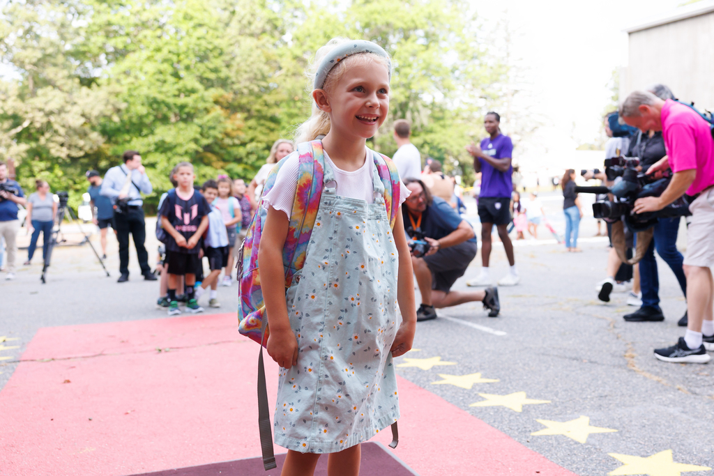 A student walks the red carpet and smiles while entering school.