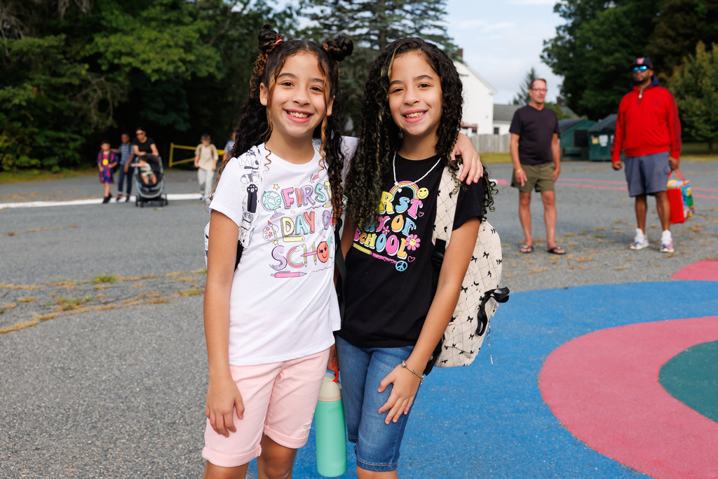 Two students wearing "First Day of School" t-shirts smile for a photo.
