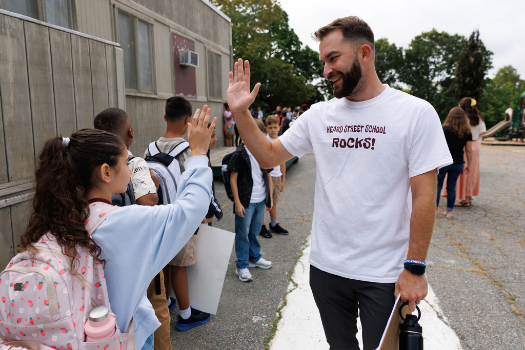 A teacher high fives a student while wearing a shirt that reads "Heard Street School Rocks" on the first day of school.