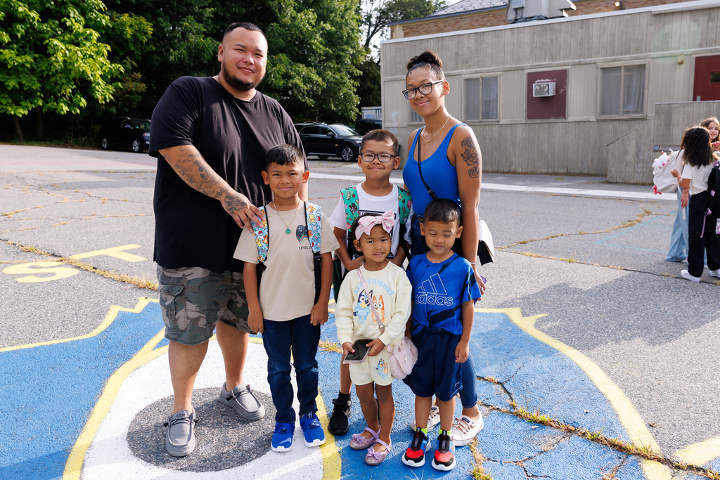 A family of five stand together and smile for a photo on the first day of school.