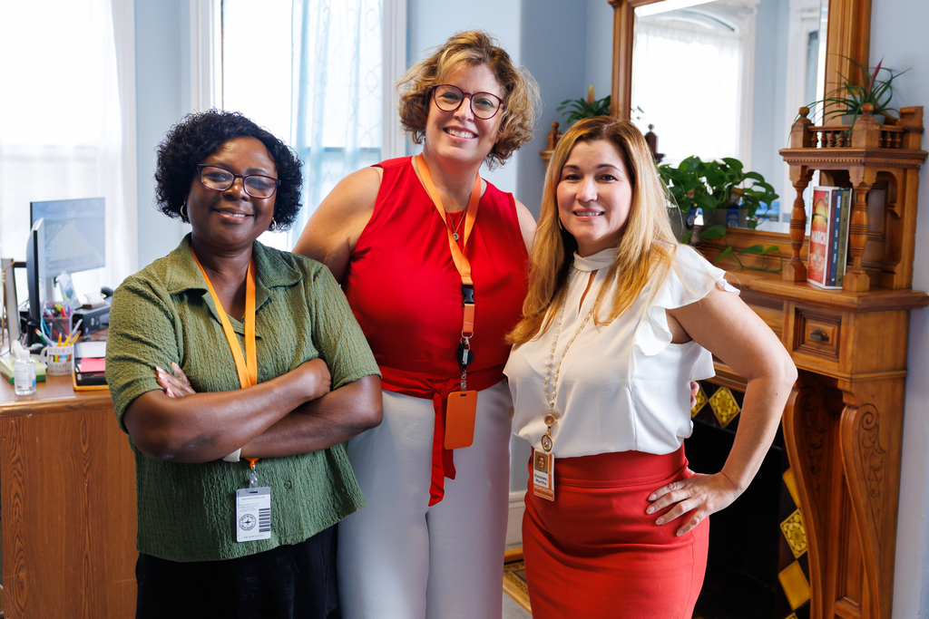 Three women smile at the camera, posing in a well-lit office setting.