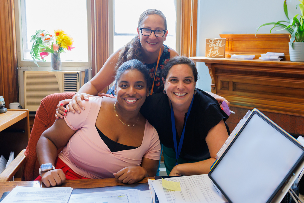 Three smiling women pose together indoors for a photo.