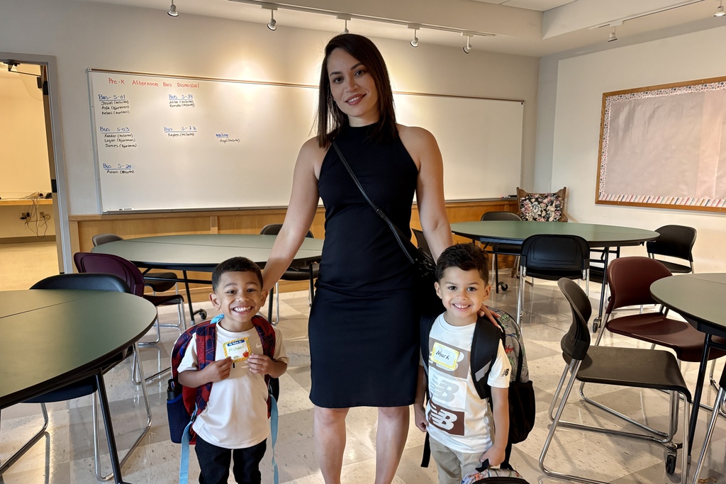 A family of three take a picture together in a classroom, all three are smiling.