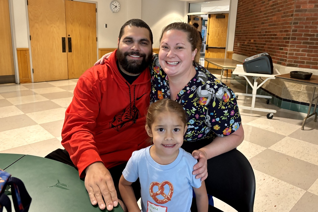 A family of three take a picture together in a classroom, all three are smiling.