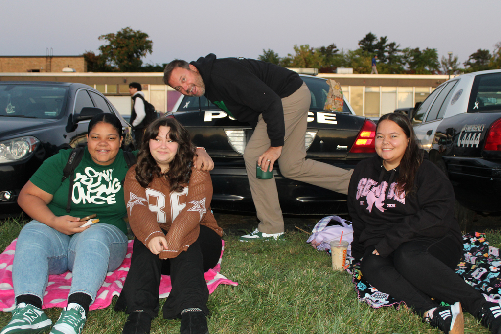 Three young people and an adult pose for a photo in front of police cars.