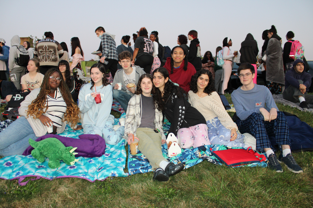 A group of diverse young people gather outdoors, sitting on blankets and enjoying each other's company.