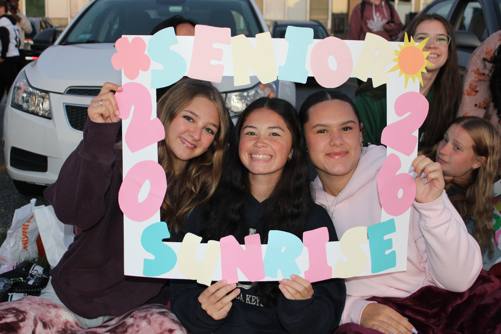 A group of smiling girls pose with a 'Senior Sunrise 2026' sign.