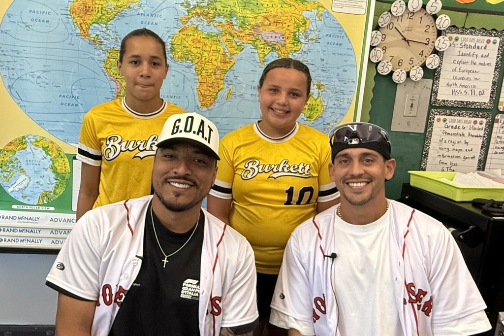 Two adults and two children pose in a classroom with a world map.