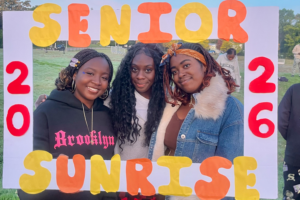 Three students holds a colorful sign that says Senior Sunrise 2026.