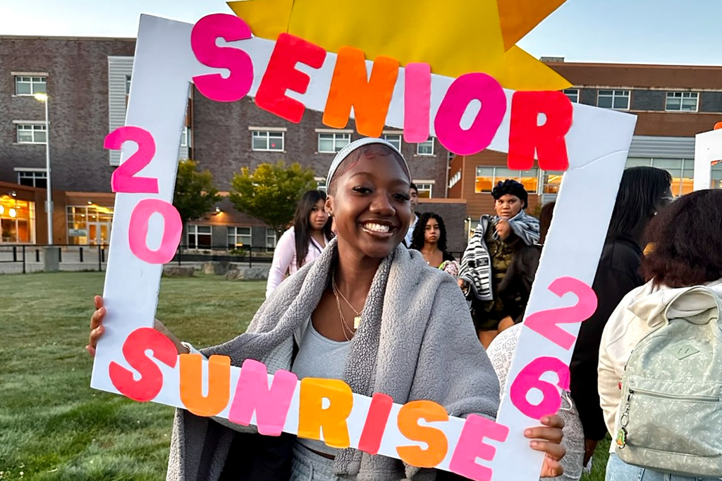 A student holds a colorful sign that says Senior Sunrise 2026.