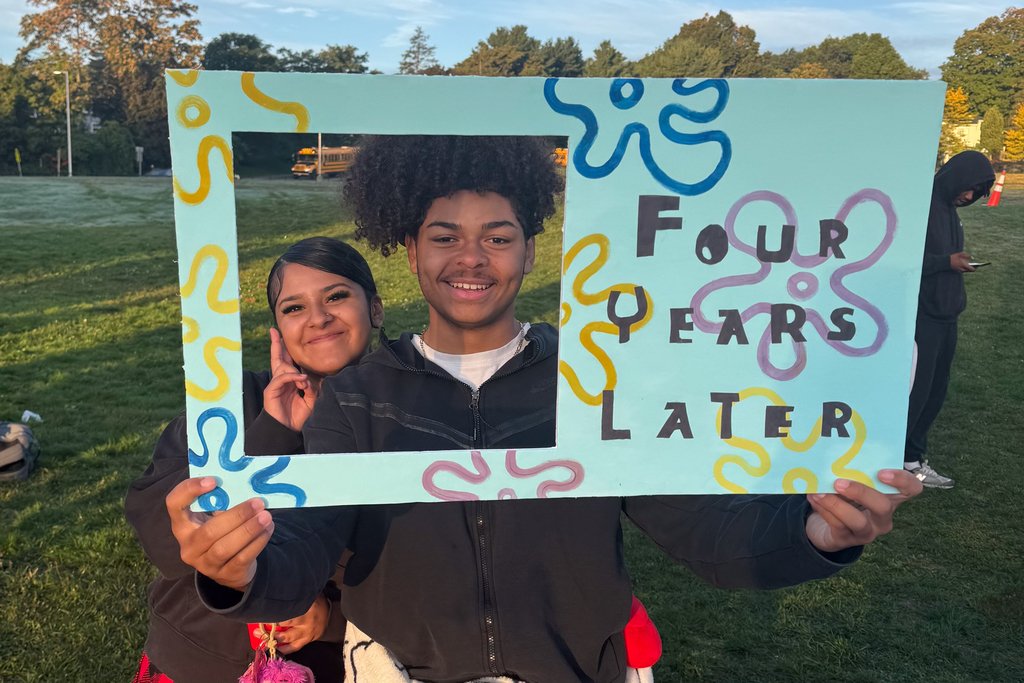 Two students hold a sign that says Four Years Later.